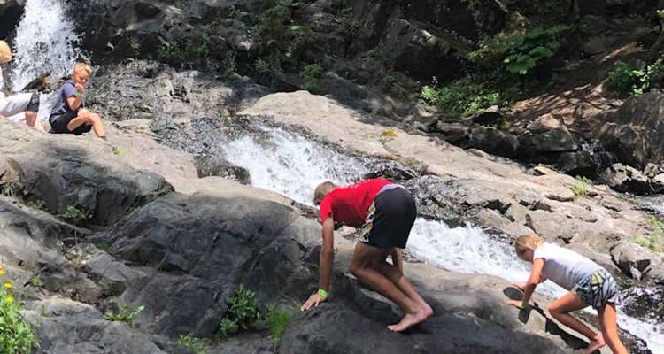 Les enfants s'empressent pieds nus sur les rochers à côté d'une cascade forestière.
