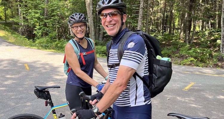 Couple heureux portant des casques se tenant avec des vélos sur une route ombragée entourée d'une forêt luxuriante.