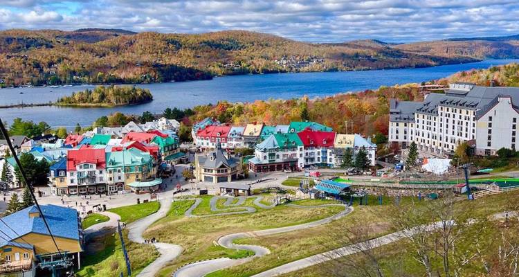 Le village coloré de style alpin de Mont-Tremblant se situe aux abords d'un lac sinueux entouré de collines forestières automnales.