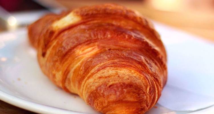 Un croissant doré repose sur une assiette blanche prêt à être dégusté.