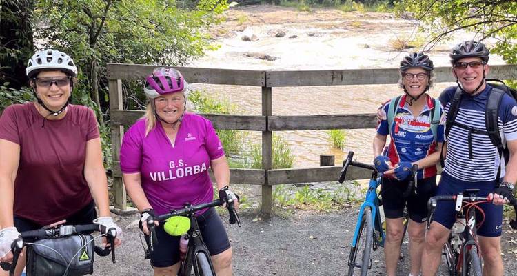 Quatre cyclistes posent avec leurs vélos à côté d'une barrière en bois surplombant une rivière aux eaux tumultueuses.