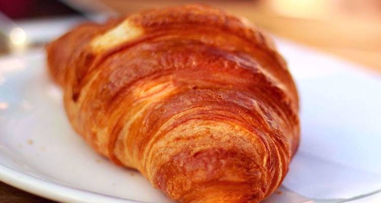 Un croissant doré et feuilleté repose sur une assiette blanche à la lumière chaleureuse.
