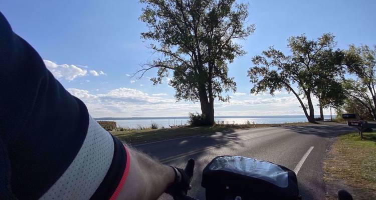 Plan subjectif d'un cycliste circulant le long d'une route au bord d'un lac avec des arbres et une étendue d'eau dégagée devant lui