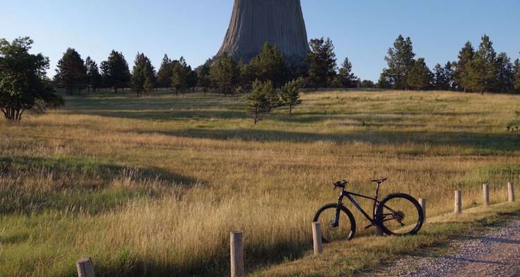 Mountainbike geparkeerd in een grasveld met Devils Tower die erachter uittorent.