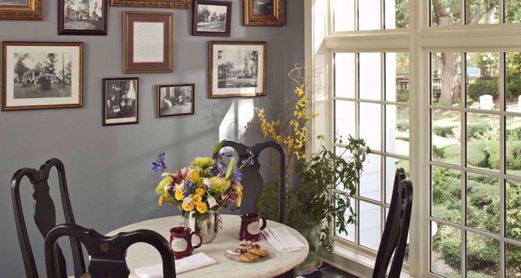 Gezellig cafetaria-hoekje met een marmeren tafel, verse bloemen en ingelijste historische foto's bij een zonnig raam
