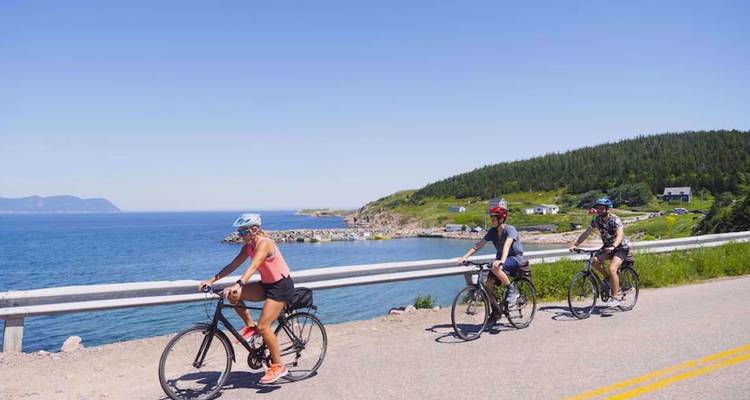 Trio de cyclistes roulant en file indienne le long d'une route côtière bordant l'Atlantique bleu éclatant.
