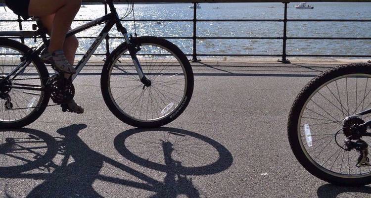 Closeup van fietswielen en fietser die schaduwen werpen op een pad langs de rivier met glitterend water