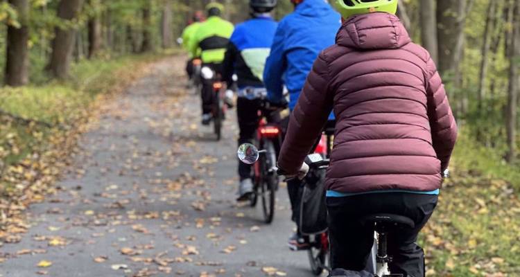Een rij fietsers in kleurrijke jacks die over een met bladeren bezaaid bospad fietsen