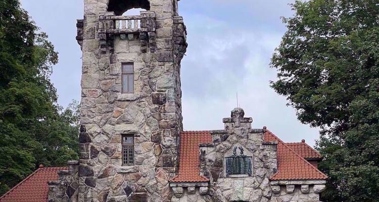 Stenen torentje in kasteelstijl met een rood pannendak en ronde ramen, omgeven door bomen