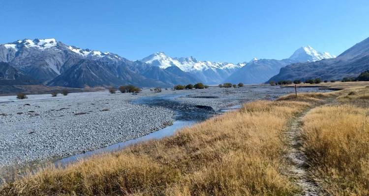 Un lit de rivière tressé s'étend sinueusement à travers une vallée dorée vers des montagnes lointaines aux pics enneigés sous des ciels dégagés.