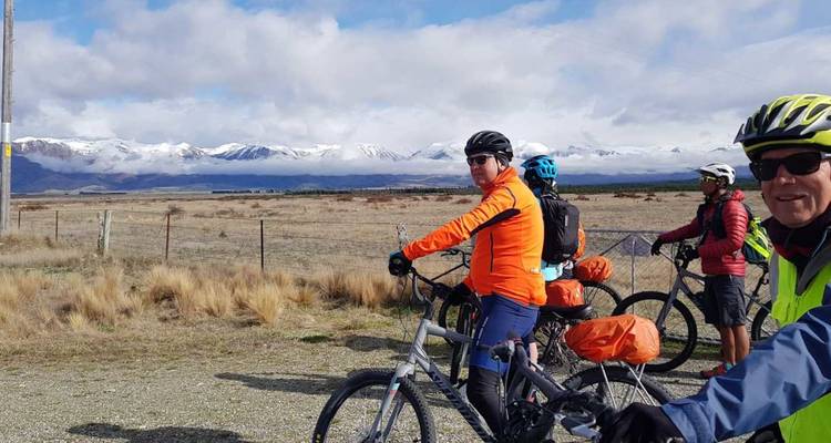 Les cyclistes s'arrêtent le long d'une piste rurale avec une chaîne de montagnes saupoudrée de neige s'étendant à l'horizon.