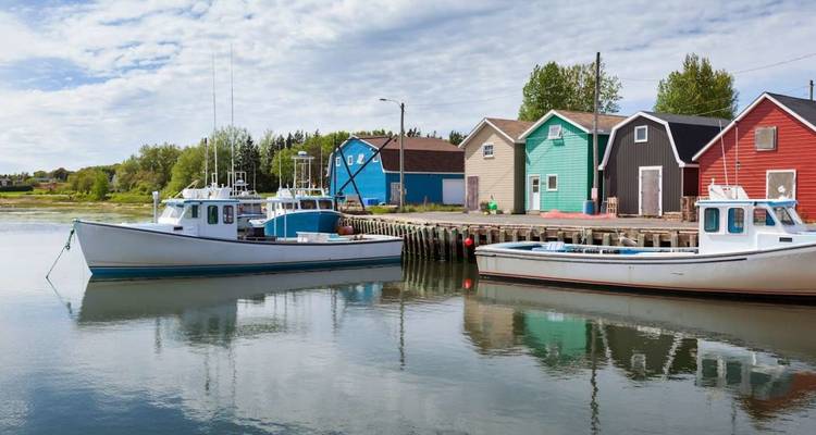 Deux bateaux de pêche blancs flottent sur un quai de village coloré dont l'image se reflète dans une eau calme.