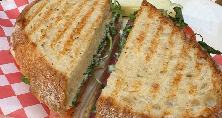 Sandwich panini grillé avec fromage fondu et verdures sur papier à carreaux.