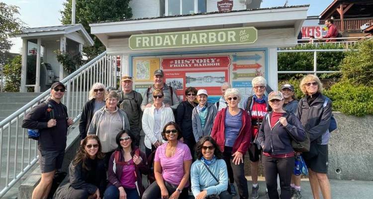 Un grand groupe de touristes sourit pour une photo devant le panneau des visiteurs de Friday Harbor.