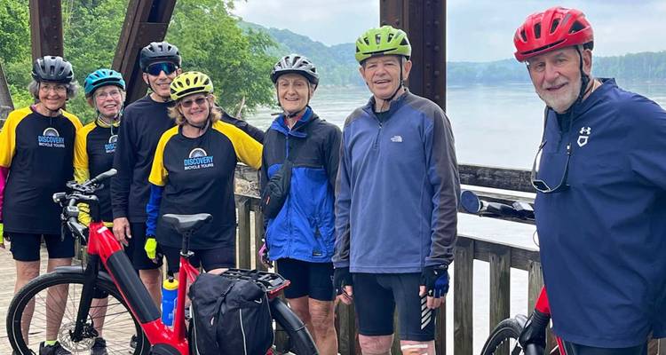 Glimlachende fietsgroep die poseert met fietsen op een houten terras met uitzicht op een rustige rivier