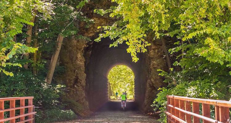Fietser die uit een stenen tunnel komt, omlijst door levendig groen loof op een bospad