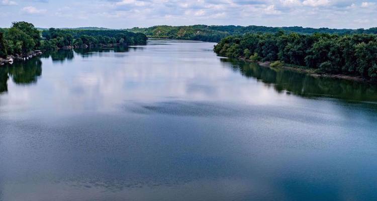 Brede rustige rivier die tussen dicht groen bos kronkelt onder een gedeeltelijk bewolkte hemel