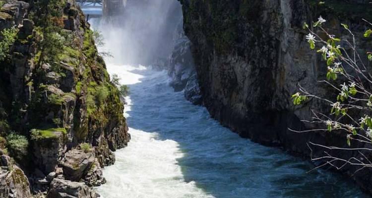 Un puissant fleuve se précipite à travers une gorge rocheuse escarpée avec de la brume s'élevant près d'un pont.