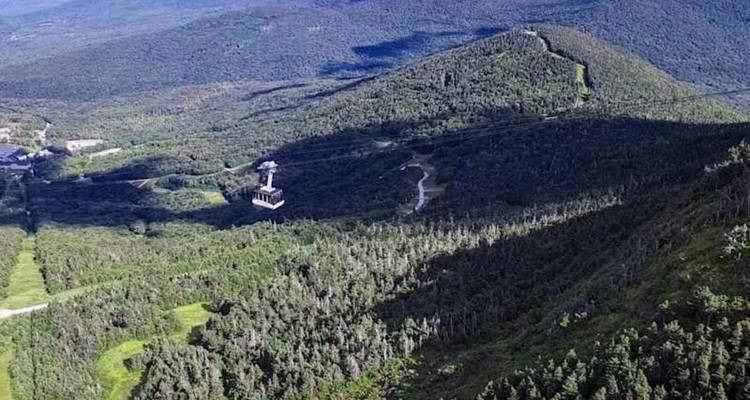 Luchtfoto van een berg met een kabelbaan die omhoog gaat over dicht bos in Vermont.