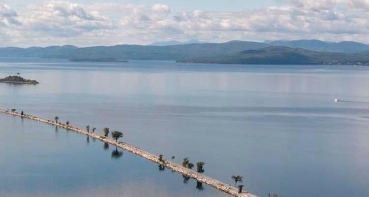 Lange stenen dijk die Lake Champlain omzoomt met bergen zichtbaar aan de overkant van het kalme water.