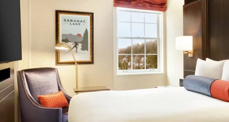 Chambre d'hôtel lumineuse et moderne avec une œuvre d'art du Saranac Lake et une grande fenêtre donnant sur les arbres.