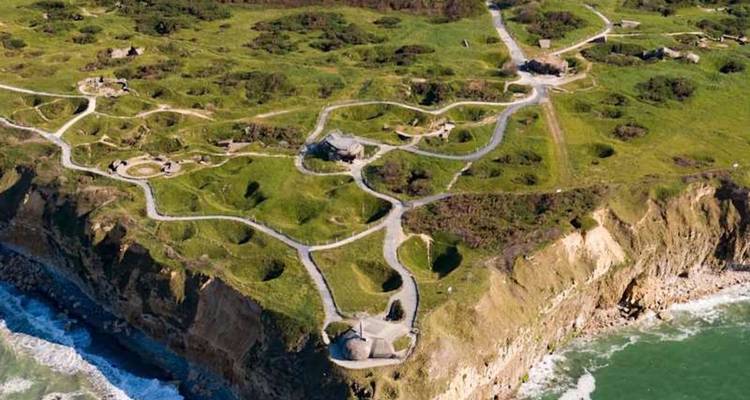 Vue aérienne des falaises de la Pointe du Hoc marquées par les bombardements, criblées de cratères et de bunkers surplombant les vagues qui s'écrasent.