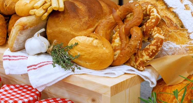 Pains artisanaux, bretzels et herbes exposés sur un étal de marché rustique en bois.