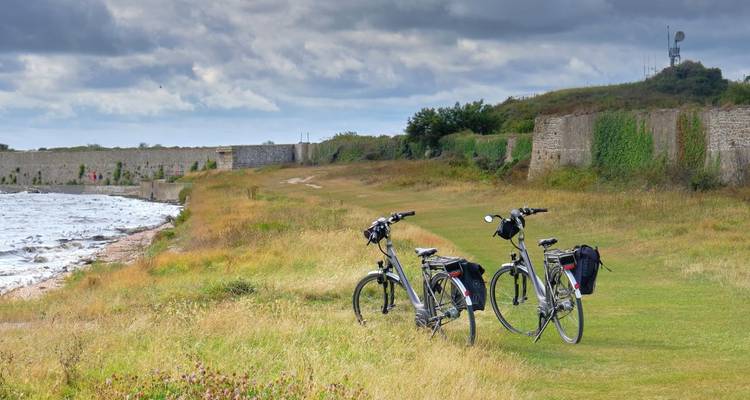 Deux vélos de randonnée reposent sur l'herbe côtière à côté des anciens murs d'un fort sous des ciels nuageux.