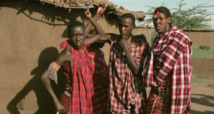 Masai-mannen in felle shukas zingen en dansen buiten traditionele leemhutten.