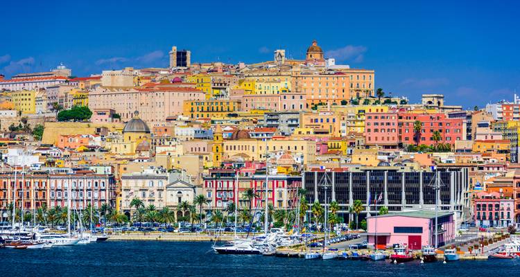 Vibrante paisaje urbano de la ladera de Cagliari con yates amarrados en la marina bajo un cielo azul profundo.