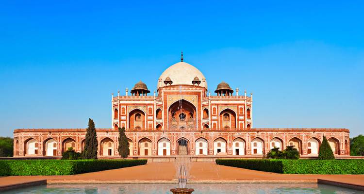 Symmetrische Ansicht des Humayun-Mausoleums, das sich in einem Vordergrundbecken unter strahlendem blauem Himmel spiegelt.