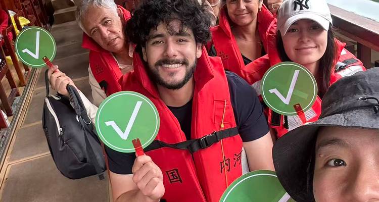 Viajeros sonrientes con chalecos salvavidas rojos sosteniendo remos con marcas de verificación verdes mientras están sentados juntos en un bote de madera.