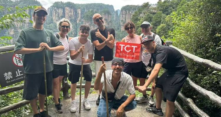 Amigos con bastones de senderismo y una bandera de tour sonríen en una plataforma de observación de madera que da vista a los imponentes pilares de arenisca del Parque Nacional de Zhangjiajie.