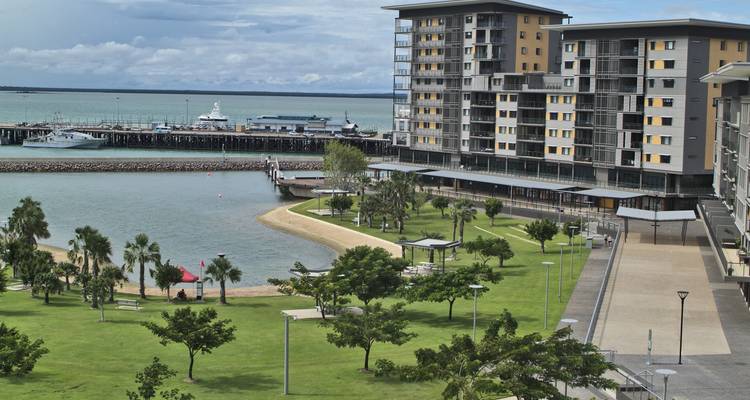 Parc côtier avec pelouses verdoyantes, palmiers, sentiers et front de mer tranquille aux eaux turquoise offrant une vue sur une marina et la mer ouverte