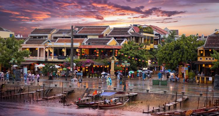 Scène de soirée pluvieuse de la Ville Ancienne de Hoi An avec des rues illuminées par des lanternes se reflétant sur le pavé mouillé au coucher du soleil.