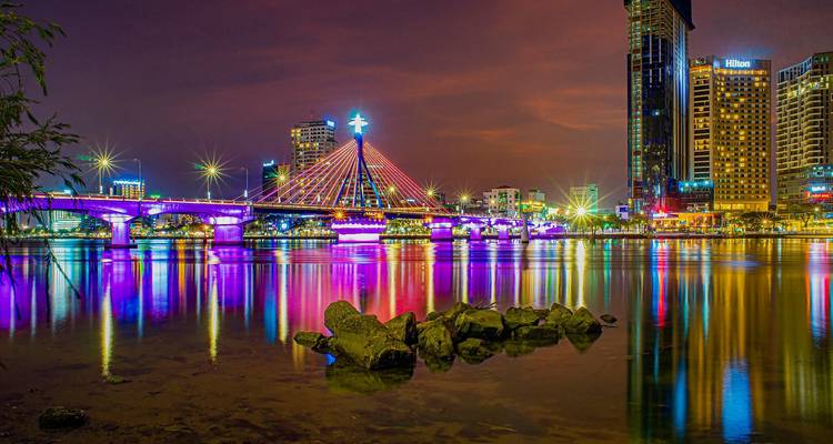 Scène nocturne colorée d'un pont à haubans illuminé à Da Nang se reflétant dans les eaux calmes de la rivière.