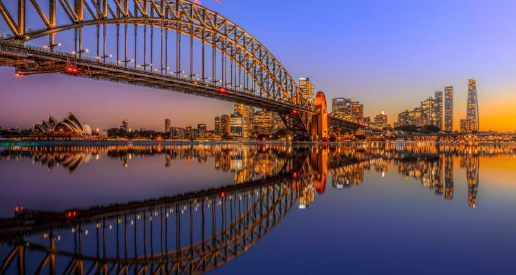 Dämmerungsblick auf die Sydney Harbour Bridge und die illuminierte Skyline, perfekt im ruhigen Wasser gespiegelt