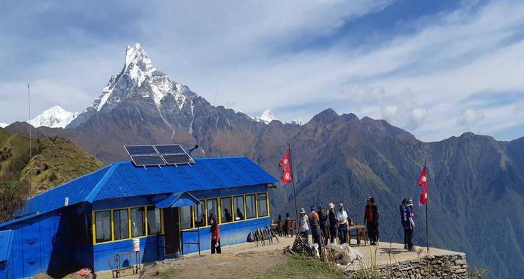 Albergue de trekking con techo azul frente al pico nevado del Machhapuchhre en la región de Annapurna.
