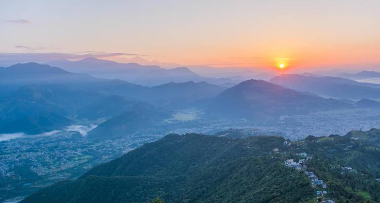 Espectacular amanecer sobre el valle de Pokhara con siluetas montañosas en capas y un sol radiante.