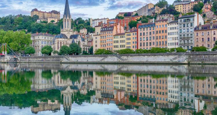 Paysage urbain coloré au bord de la rivière avec clocher d'église et reflets parfaits des bâtiments dans l'eau calme.