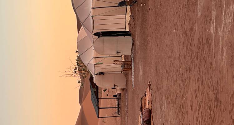 Des tentes de camp désertique simples au crépuscule avec un ciel aux teintes pastel douces au-dessus du sol sablonneux.