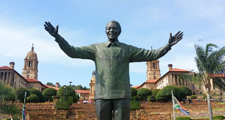 Grande statue en bronze de Nelson Mandela avec les bras écartés dans un jardin formel.