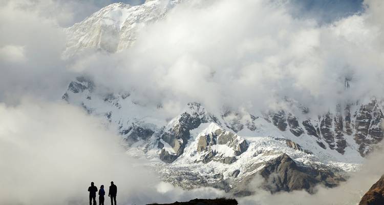 Trois trekkeurs en silhouette contre des nuages dérivant sur une face neigeuse dramatique de l'Himalaya