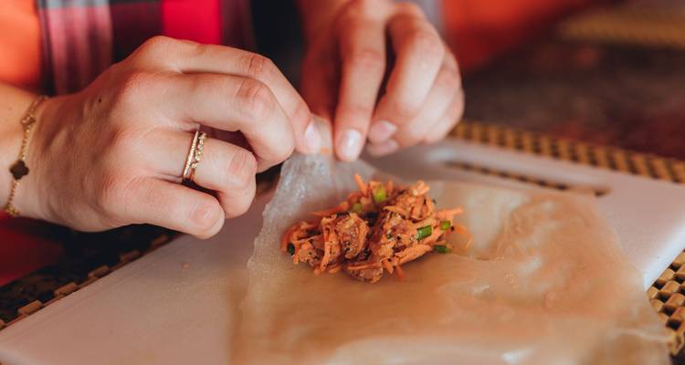Gros plan des mains préparant des rouleaux de printemps frais sur une planche à découper lors d'un cours de cuisine