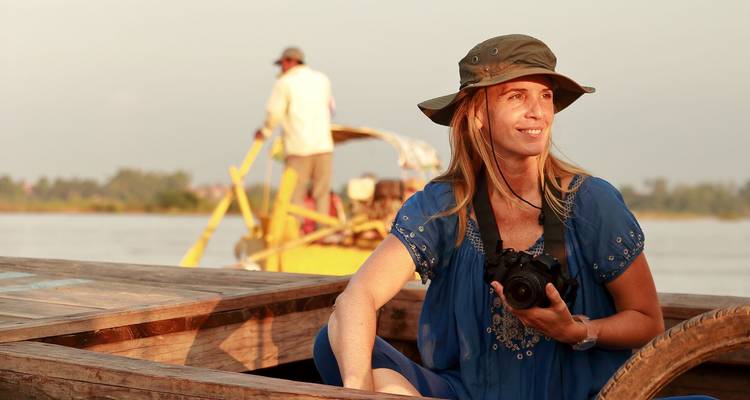 Femme avec appareil photo souriante à bord d'un bateau en bois sur un large fleuve à l'heure dorée