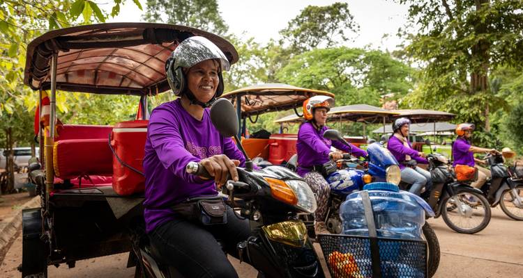 Ligne de conducteurs de tuk-tuk en uniformes violets souriants en attente sur des motos sous des arbres luxuriants