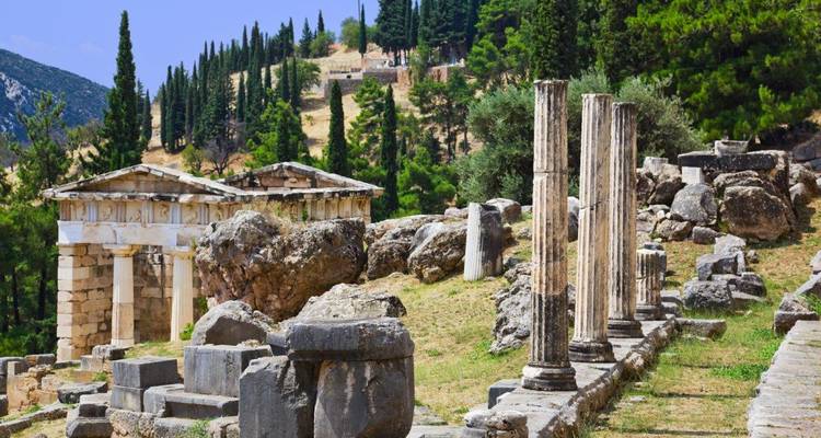 Klassieke ruïnes in Delphi met staande zuilen en heuvels bedekt met cipressen op de achtergrond.