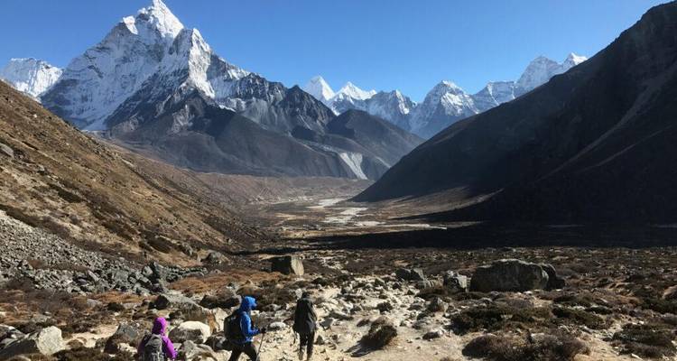 Los excursionistas hacen una pausa en un enorme valle himalayo rodeado de picos nevados dentados bajo un cielo despejado.