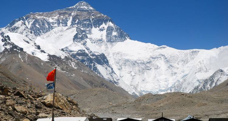 Vista lejana de la cara norte del Everest elevándose sobre llanuras áridas de gran altitud y carpas de expedición.