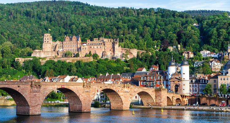Puente antiguo y Castillo de Heidelberg capturados juntos al otro lado del río que brilla bajo un cielo radiante.